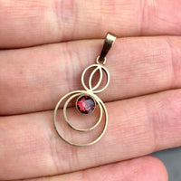 A Petite Art Deco 9ct Gold Garnet Circular Drop Pendant in hand