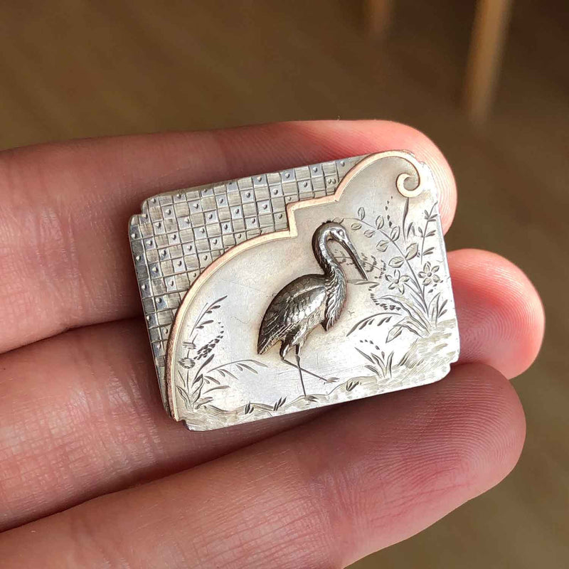 Victorian Aesthetic Silver and Gold Brooch featuring a Heron. c1890 in a hand - Jewellery Hound